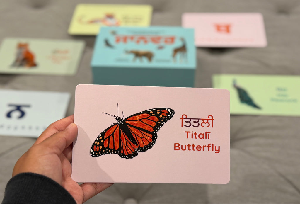 Hand holding a card with a butterfly illustration and text on a gray surface with other cards in the background.